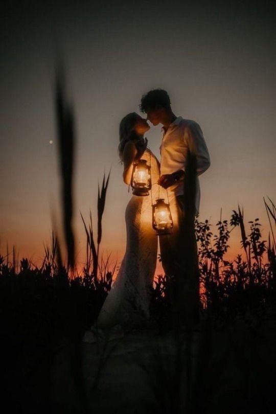 A couple holding lanterns in the field at dusk